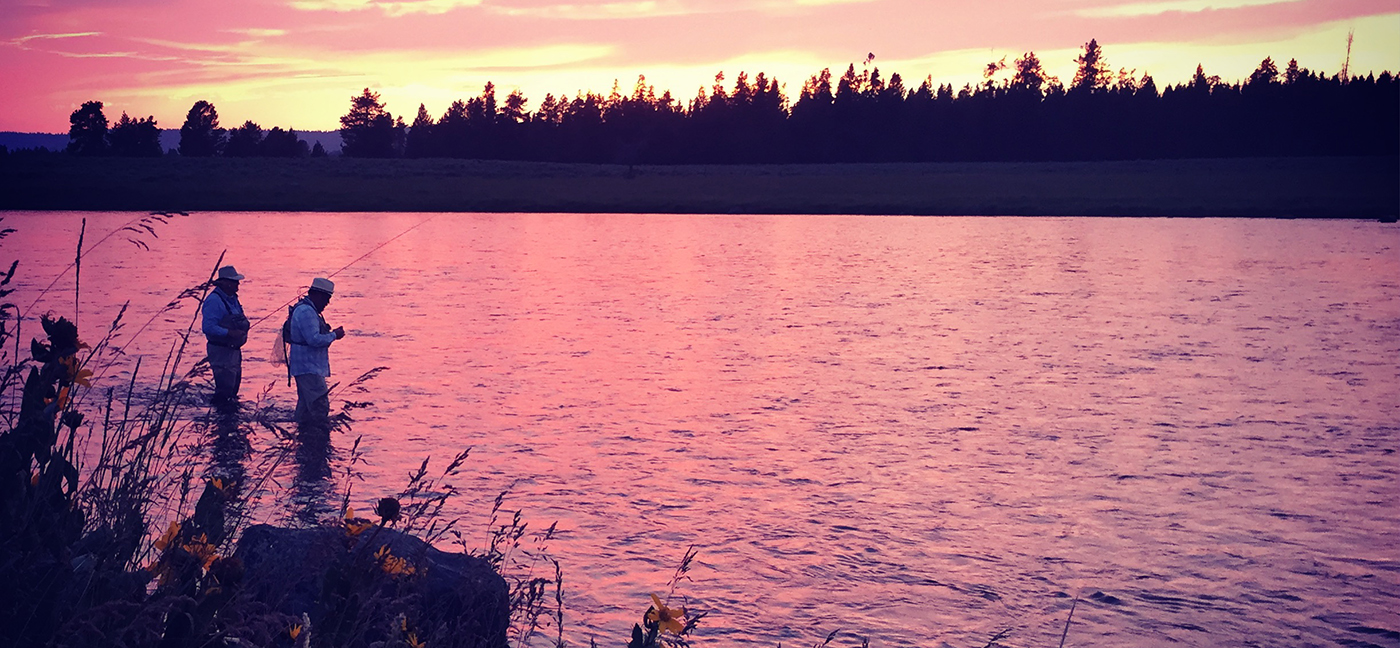 Two fly fishermen silhouetted against a sunset sky