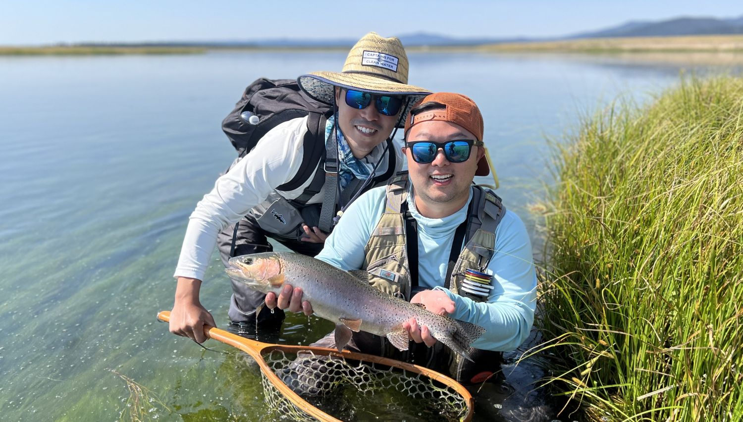 Two fly fisherman hold up a large rainbow trout